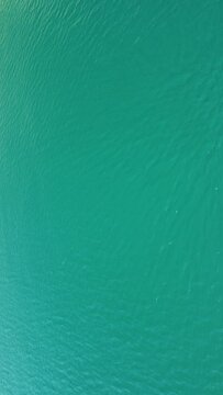Vertical aerial view on sea water surface, camera flies over clear sea water. Sun glare. Abstract nautical summer ocean nature. Holiday, vacation and travel concept. Nobody. Vertical video
