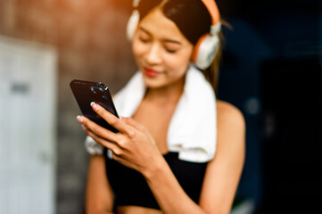 Asian woman wearing fitness clothes Play on the phone, wear white headphones, listen to music, relax during exercise, generate energy for exercise inspiration.
