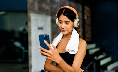 Asian woman wearing fitness clothes Play on the phone, wear white headphones, listen to music, relax during exercise, generate energy for exercise inspiration.