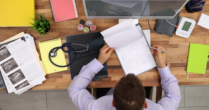 Doctor male internist cardiologist filling out medical form in clinic. Medic writes personal information