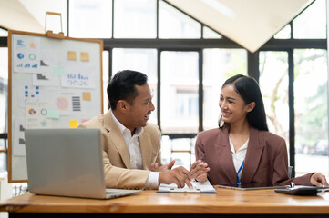 A happy Asian businessman is sharing ideas, brainstorming, and working with a female colleague
