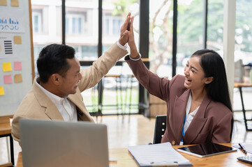 A happy Asian businessman is giving high fives to a female colleague to cheer her up
