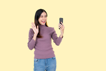 Fototapeta premium A positive Asian woman enjoys talking on a video call, isolated yellow background.