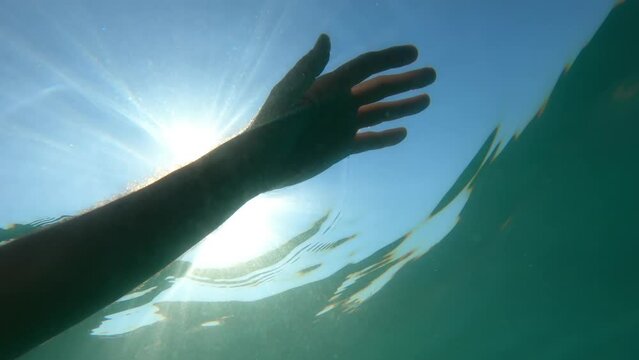 Hand of a drowned man floating in ocean water back lit by the hot summer sun, underwater shot, conceptual footage
