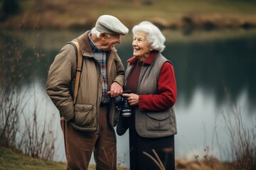Naklejka na ściany i meble A happy elderly couple walks through the park with a camera and laughs