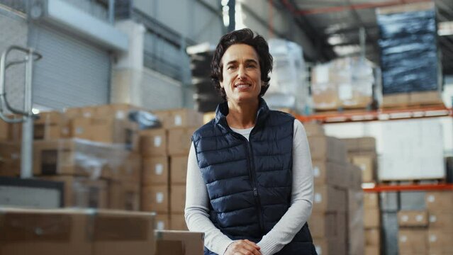 Female warehouse worker smiles at the camera while standing next to boxes of inventory, she is an essential part of the fulfilment center, with experience in managing the flow of goods and fulfilment.