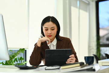 Focused asian woman entrepreneur using digital tablet working on investment and marketing projects at office