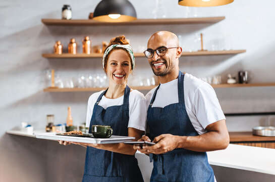 Two happy waiters standing together in a cafe, ready to serve customers