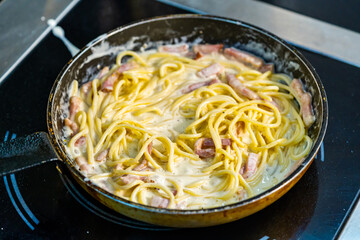 A pan filled with pasta and bacon on top of a stove. Delicious pasta dish cooking on the stove