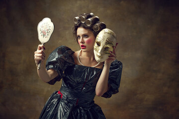 Portrait of young woman dressed in black dress made of garbage bags curls hair with paper tubes...