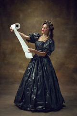 Full lenght portrait of woman wearing in black dress made of garbage bags curls hair with paper...