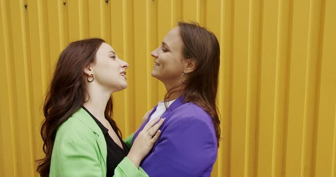 LGBT Female talking and dancing in colorful clothes outdoors on wellow background. Young woman hugging and kissing happy girlfriend. Love and kiss, Romance and portrait of lesbian couple enjoying.