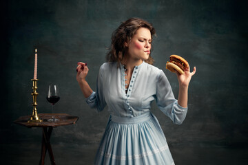 Princess. Portrait of aristocratic hungry woman wearing blue historical dress eating big hamburger....