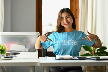 Positive young woman, volunteer pointing fingers at blue t-shirt and smiling to camera
