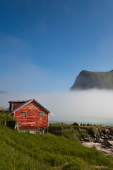 Fototapeta na wymiar Red norwegian house in a fjord on a bright sunny morning, with fog clouds rolling in from the sea