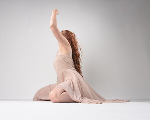 Obraz premium Full length portrait of beautiful brunette model wearing a pink dress. graceful sitting pose, kneeling on floor gestural hands. shot from low angle perspective, isolated on white studio background