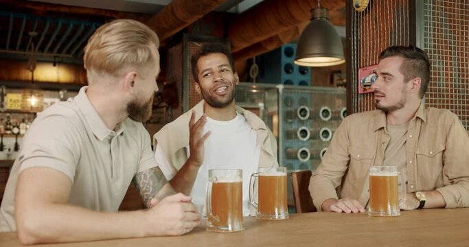 Male colleagues in good mood drinking draft beer and relaxing. Concept of friendship and leisure. Young people enjoying themselves and communicating in pub concept.