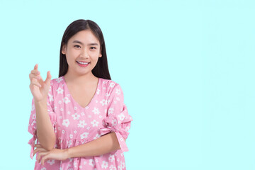 Young preetty Asian beautiful female with black long hair in pink shirt shows present something while isolated on light blue background.