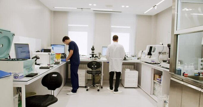 Men working in clinic laboratory. Handheld shot of male medical specialists in uniform preparing samples and using analyzing machine during work in lab of modern hospital.