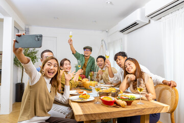 Group of Cheerful Asian man and woman using mobile phone taking selfie together during celebration dinner party at home. Happy people friends enjoy and fun reunion meeting holiday event on vacation. - obrazy, fototapety, plakaty