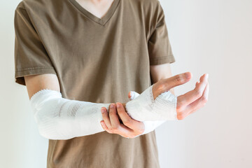 Young man with gauze bandage wrapped around his injured arms, knee at home. Man with hands wrap in medical bandage on white background. First aid, treatment after accident injury. Copy space, closeup