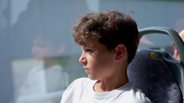 reflective young boy on bus, lost in distant gaze. Youthful traveler settled in seat, exuding deep pondering serious expression