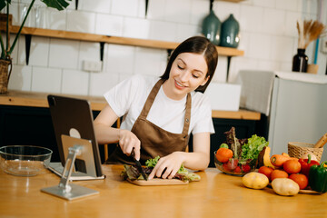 Young American woman learning online cooking class via tablet computer in kitchen
