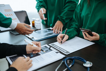 Medical team having a meeting with doctors in white lab coats and surgical scrubs seated at a table discussing a patients working online using computers in the medical industry.