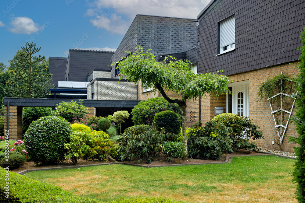 Poster house with tree in the middle of the yard and bushes in front of it in germany.