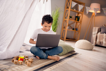 Portrait of nice cheerful cute little boy sit floor play computer video game wear white shirt light modern room interior design apartment © deagreez