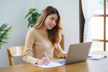Obraz premium Happy beautiful Asian woman using computer laptop for work online at living room.