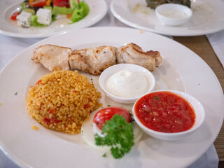 grilled chicken and fried rice and tomato source and sour cream on the white plate in tatar restaurant in capital kyiv