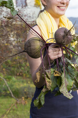 Young woman holds two red beetroots in her hand. Fresh havested vegetables with soil rests and leaves on them.