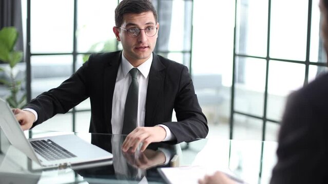 Thoughtful diverse colleagues sit at desk in office talk discuss business ideas at briefing together,