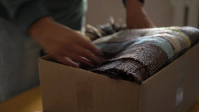 Volunteer stacking warm plaid blankets in a donation box. Donate. 
moving. Woman folding clothes, close up
