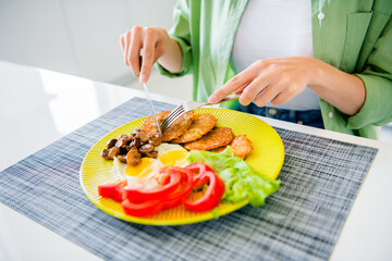 Cropped portrait of girl hands hold fork knife homemade dish plate fried eggs cutlets meat fresh vegetables kitchen house inside
