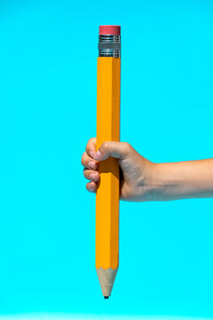 Crop person holding large yellow pencil in blue studio