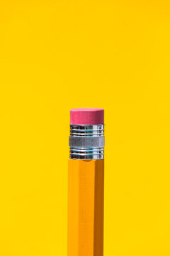 Bright yellow pencil with eraser on top in blue studio