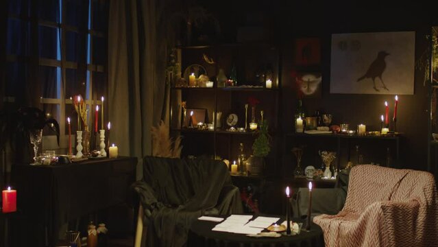Medium long view of fortune teller dark room studio with lots of candles, posters and place for working with clients