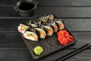Sushi roll futomaki with cucumber and fried salmon on a black stone plate served with soy sauce and ginger