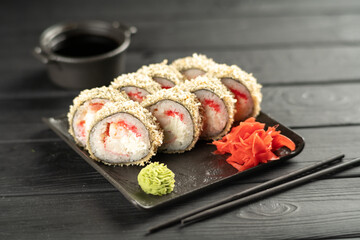 Fried hot sushi roll with shrimp, smoked eel, cream cheese with chopsticks and sauce on black background. Sushi menu. Japanese food concept.