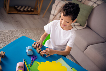 Photo of sweet pretty little boy dressed white t-shirt sitting table making words letter cubes indoors house home room