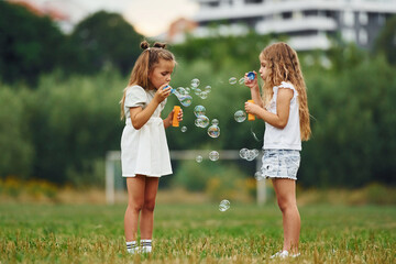 Two girls are playing with bubbles together on the green field