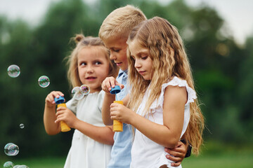 Fototapeta premium With bubbles. Kids are having fun on the field at daytime together