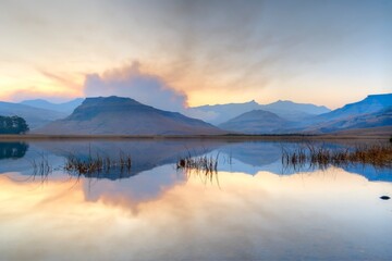 SMOKE FROM A WINTER GRASSFIRE reflects in a drakensberg mountain lake - 633336081