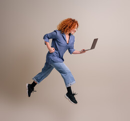 Young businesswoman with curly hair working over laptop and jumping in air over background