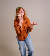 Cheerful beautiful woman laughing and talking over smart phone while standing on background