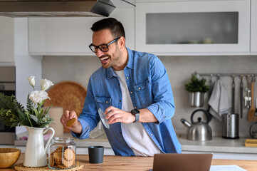 Young businessman laughing and taking cookies from jar with coffee cup on kitchen counter at home