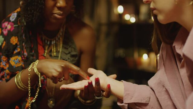 Medium close up of fortune teller reading palm of female client eager to know her destiny sitting at seance in studio