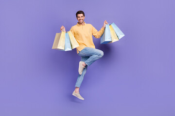 Full body photo of jump satisfied young fashion designer man holding bargains purchase new packages isolated over violet color background